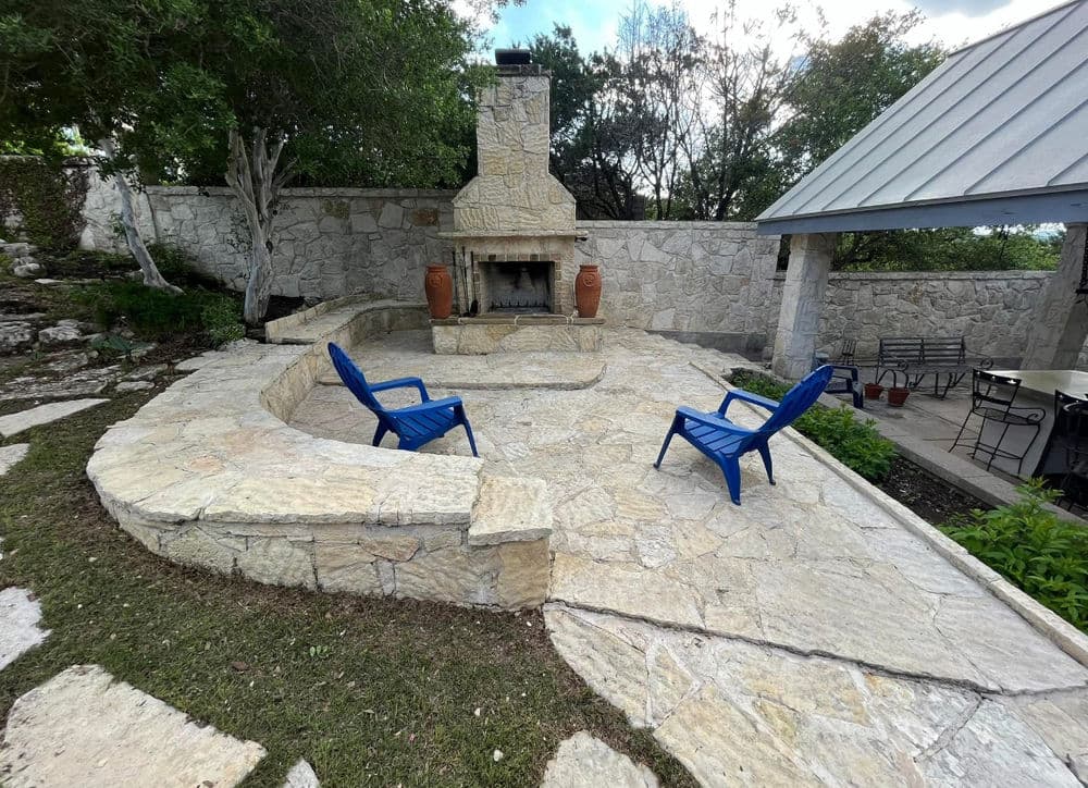 Outdoor stone patio featuring a fireplace and surrounding greenery, perfect for gatherings.